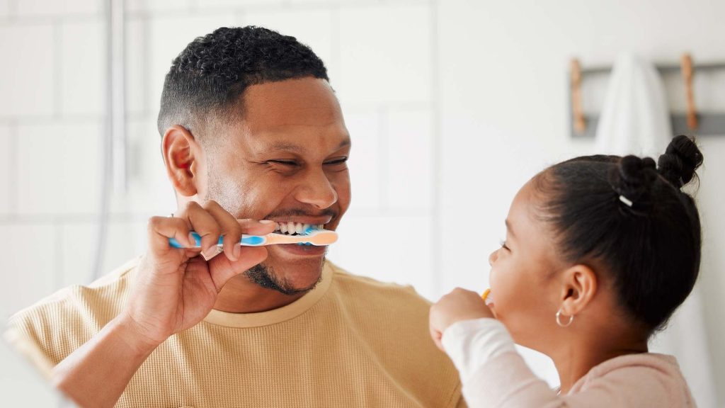Father, child and brushing teeth in a family home bathroom for dental health and wellness in a mirror.